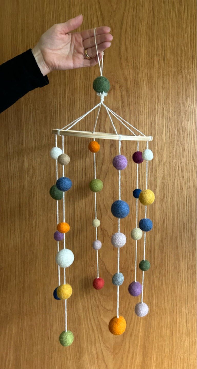 Bunte Kugel-Mobile an einem Drahtgestell, sanft hängend von einer Hand gehalten.