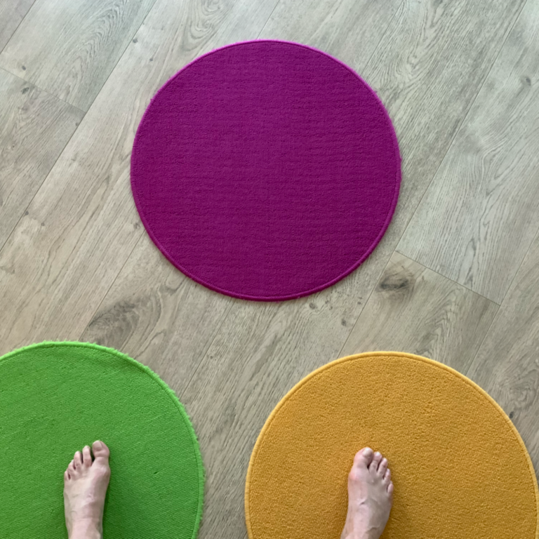 Füße stehen auf bunten, runden Teppichen in den Farben lila, grün und orange. Die drei Teppiche stehen Symbolisch für drei Möglichkeiten.