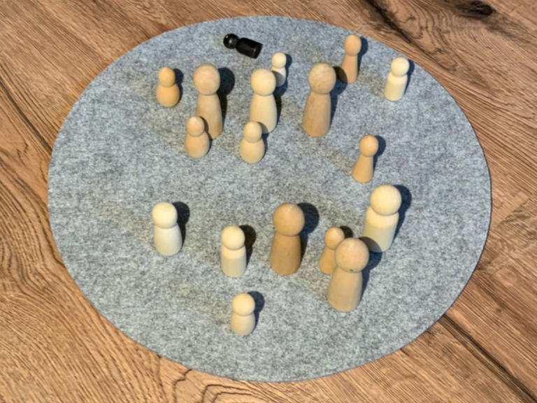 Holzfiguren in verschiedenen Größen auf einem grauen, runden Filzuntergrund.