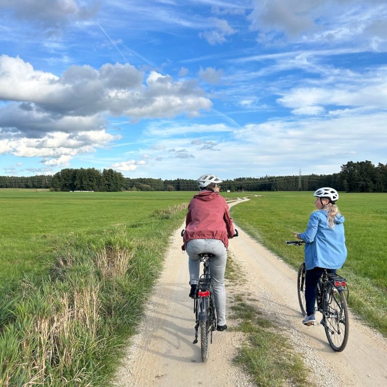 Zwei Personen auf Fahrrädern entlang eines Feldwegs unter einem blauen Himmel.