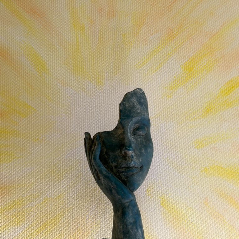 Eine stilisierte Skulptur einer Hand mit einem Gesicht, vor einer stilisierten gemalten Sonne. 